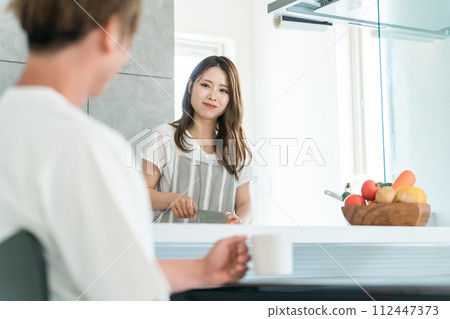 一對微笑的年輕亞洲夫婦在自家廚房做飯和做家務時交談 112447373