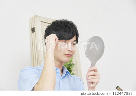 Young man looking in the mirror and adjusting his hairstyle 112447885