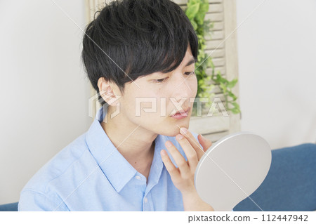 一個年輕人照鏡子，擔心未剃的頭髮 112447942