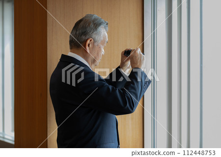 高級商人用雙筒望遠鏡觀察下面的建築物 高級商人用雙筒望遠鏡觀察下面的建築物 112448753