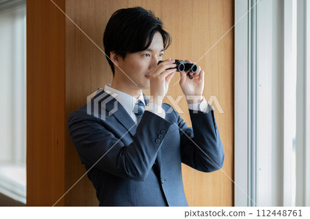 Businessman looking at the building below with binoculars 112448761