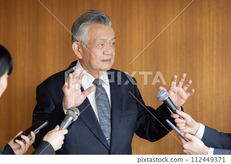 Senior businessman responding to questions from reporters 112449371
