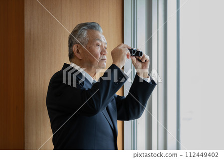 Senior businessman looking into the building below with binoculars 112449402