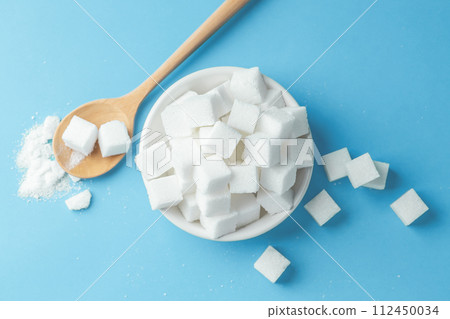 White sugar cubes in bowl with spoon on blue background, top view White sugar cubes in bowl with spoon on blue background, top view 112450034