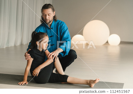 A yoga instructor in training helps a child to do exercises in the gym A yoga instructor in training helps a child to do exercises in the gym 112451567