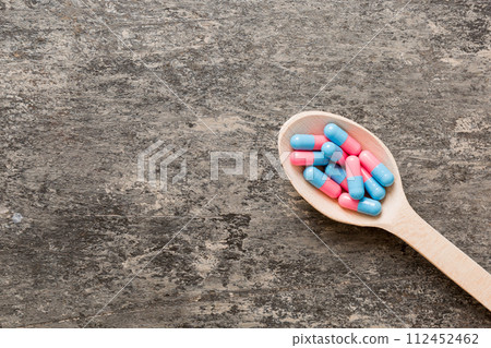 Vitamin capsules in a spoon on a colored background. Pills served as a healthy meal. Red soft gel vitamin supplement capsules on spoon 112452462