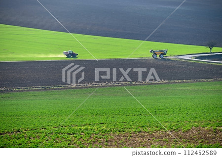 Tractor in the field in spring time. Green field in spring and work on cultivating the soil. Concept for agriculture. 112452589