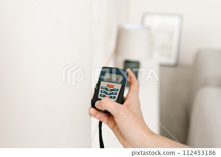 Laser rangefinder in the hands of a woman. An engineer holding a laser rangefinder. Close up of a measuring device in a house. Designer using an electronic rangefinder in a room 112453186