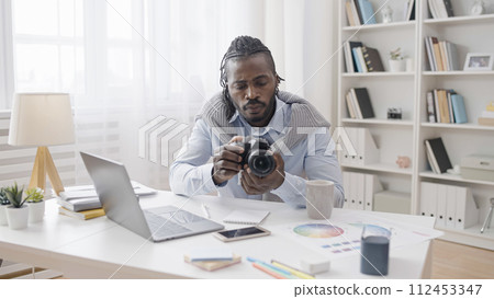 A male artist is adjusting his new professional photo camera and watching a tutorial on his laptop 112453347