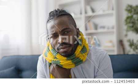 Portrait of sad African American man in scarf feeling cold, flu or coronavirus symptoms Portrait of sad African American man in scarf feeling cold, flu or coronavirus symptoms 112453403