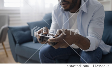 Close-up of excited man playing video game with wireless joystick at home, relaxation 112453406
