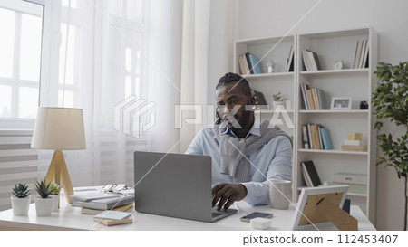 Serious African American man working on laptop at home, freelancer, business owner Serious African American man working on laptop at home, freelancer, business owner 112453407