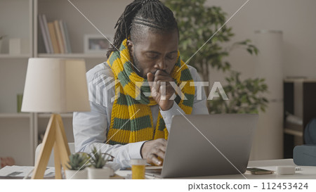 African American man in scarf coughing while working on laptop, flu, common cold 112453424
