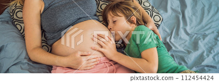 BANNER, LONG FORMAT Young beautiful pregnant woman and eldest son. The cute boy leaned his ear against his mother's belly. Expecting a baby in the family concept. Preparing an older child for a BANNER, LONG FORMAT Young beautiful pregnant woman and eldest son. The cute boy leaned his ear against his mother's belly. Expecting a baby in the family concept. Preparing an older child for a 112454424