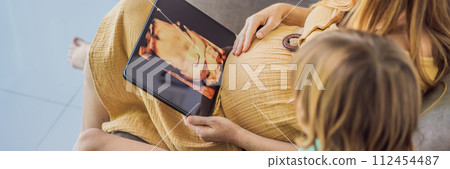 Mom and her son looking on ultrasound image of his unborn baby brother on mothers tablet. Concept of healthcare and family happiness expecting baby BANNER, LONG FORMAT 112454487