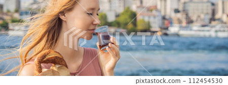 BANNER, LONG FORMAT Woman in Istanbul having breakfast with Simit and a glass of Turkish tea. Glass of Turkish tea and bagel Simit against golden horn bay and the Galata Tower in Istanbul, Turkey BANNER, LONG FORMAT Woman in Istanbul having breakfast with Simit and a glass of Turkish tea. Glass of Turkish tea and bagel Simit against golden horn bay and the Galata Tower in Istanbul, Turkey 112454530