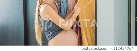 BANNER, LONG FORMAT A pregnant woman has nothing to wear. A pregnant woman stands in front of a closet with clothes and does not know what to wear because the clothes do not fit on her BANNER, LONG FORMAT A pregnant woman has nothing to wear. A pregnant woman stands in front of a closet with clothes and does not know what to wear because the clothes do not fit on her 112454764