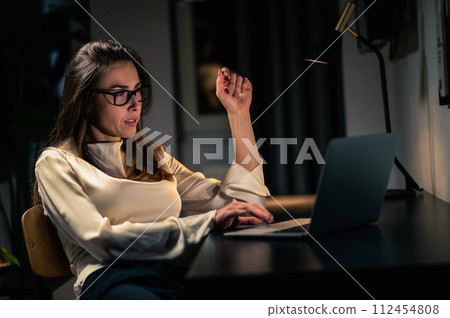 Woman using laptop having online video call at home at night in dark room Woman using laptop having online video call at home at night in dark room 112454808