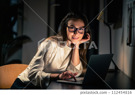 Woman using laptop for remote working at home at night in dark room Woman using laptop for remote working at home at night in dark room 112454816