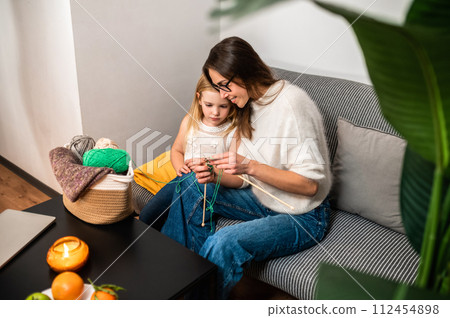 Young woman knitting with her daughter in cozy living room at home Young woman knitting with her daughter in cozy living room at home 112454898