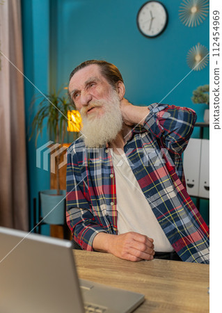 Senior elderly man suffers from spine neck muscle pain at home office workplace working on laptop 112454969