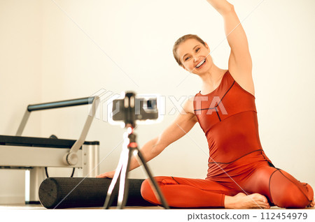 Woman yoga instructor recording online training with smartphone and tripod in fitness studio 112454979