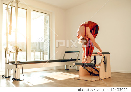 Woman in sports wear having workout on reformer machine in yoga studio Woman in sports wear having workout on reformer machine in yoga studio 112455021