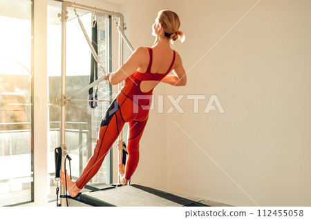 Attractive slim woman training her sporty body on the Pilates machine Attractive slim woman training her sporty body on the Pilates machine 112455058