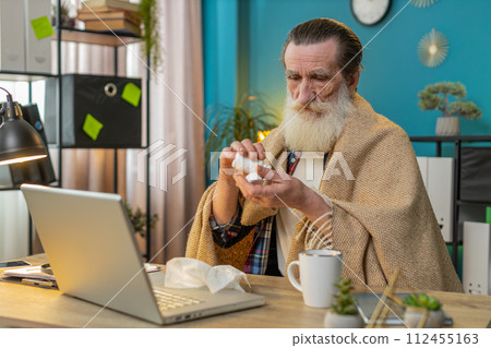 Sick ill senior man suffering from cold flu allergy blows sneezes wipes snot works on laptop at home Sick ill senior man suffering from cold flu allergy blows sneezes wipes snot works on laptop at home 112455163