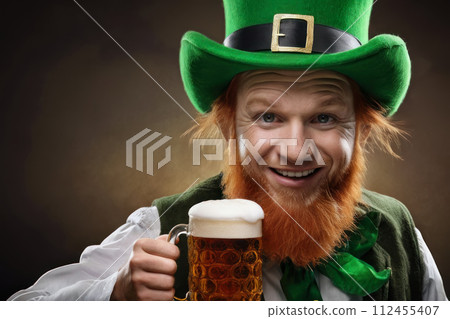 smiling redhead man with beard in green suit and leprechaun hat holding mug of beer. St. Patrick's Day celebration 112455407