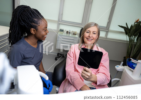 Woman patient looking at mirror with smile in dentist s office Woman patient looking at mirror with smile in dentist s office 112456085