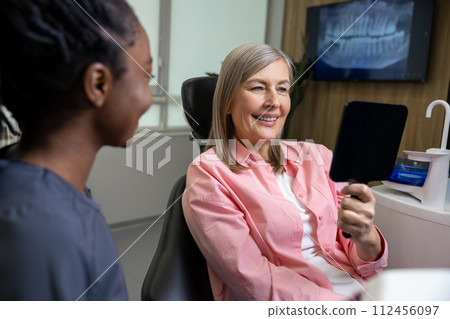 Caucasian lady checking her beautiful smile in mirror after stomatology treatment Caucasian lady checking her beautiful smile in mirror after stomatology treatment 112456097