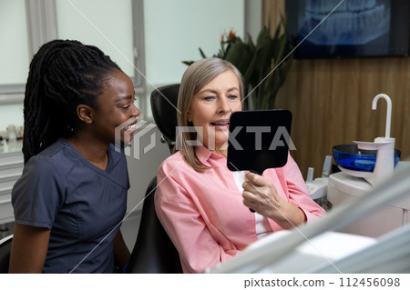 Middle aged woman patient looking at her new dental implants in mirror Middle aged woman patient looking at her new dental implants in mirror 112456098
