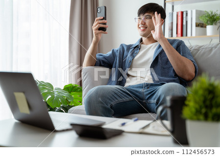 Cheerful happy Young Asian man using smart phone for online video conference call talking happily. Cheerful happy Young Asian man using smart phone for online video conference call talking happily. 112456573