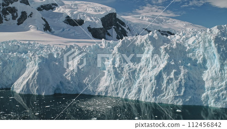 Mountain glacier with snow and ice at ocean bay aerial. White icy and snowy desert nature seascape at frozen dark blue water. Melting icebergs and climate change scenery. Epic arctic winter landscape 112456842