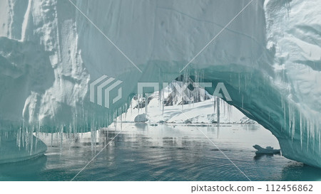 Close up iceberg arch at ocean bay aerial. Amazing environment of polar winter at snow covered mountains ridges. Nobody nature of arctic seascape. Global warming, climate change scene Close up iceberg arch at ocean bay aerial. Amazing environment of polar winter at snow covered mountains ridges. Nobody nature of arctic seascape. Global warming, climate change scene 112456862