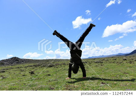 Woman hiker doing a handstand on high altitude mountain meadow Woman hiker doing a handstand on high altitude mountain meadow 112457244