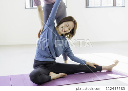 A middle-aged woman looks in pain as her arm is pulled by the instructor during a yoga lesson. 112457383