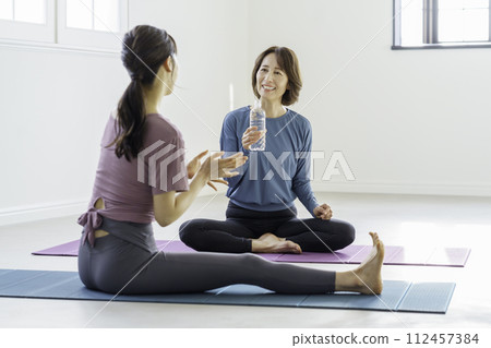Yoga lesson: middle-aged woman drinking water with instructor during break 112457384