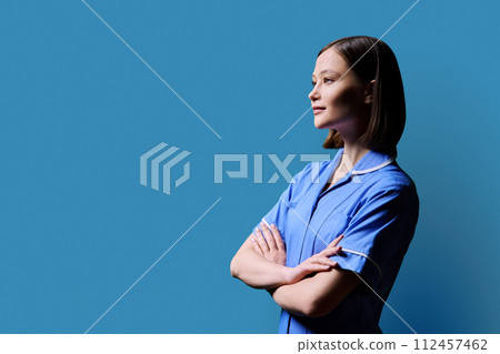 Portrait of young serious female nurse looking in profile on blue background 112457462
