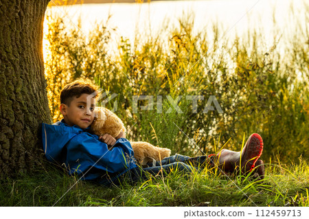 Thoughtful Child with Plush Toy Resting Against Tree 112459713
