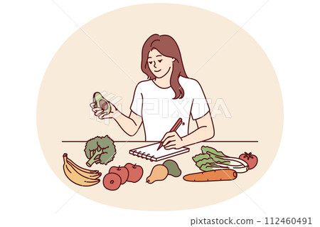 Woman near table with vegetables makes notes counting calories or making plan for new keto diet 112460491