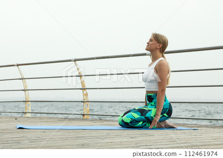 Young woman on yoga mat on wooden floor outdoors, space for text 112461974
