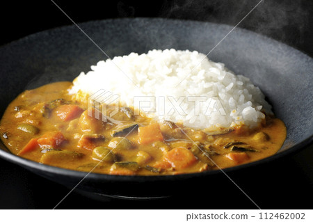 A photo of piping hot curry rice with plenty of vegetables such as pork, pumpkin, and carrots against a black background. 112462002
