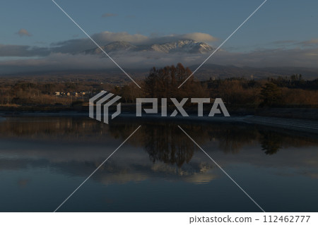 Irrigation water pond reflecting the snowy Mt. Yatsugatake with dawn clouds Irrigation water pond reflecting the snowy Mt. Yatsugatake with dawn clouds 112462777