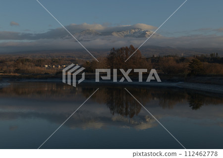 Irrigation water pond reflecting the snowy Mt. Yatsugatake with dawn clouds 112462778