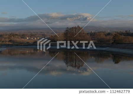 Irrigation water pond reflecting the snowy Mt. Yatsugatake with dawn clouds Irrigation water pond reflecting the snowy Mt. Yatsugatake with dawn clouds 112462779