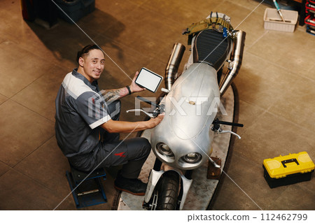 Smiling repairman using application on tablet computer when examining motorcycle Smiling repairman using application on tablet computer when examining motorcycle 112462799