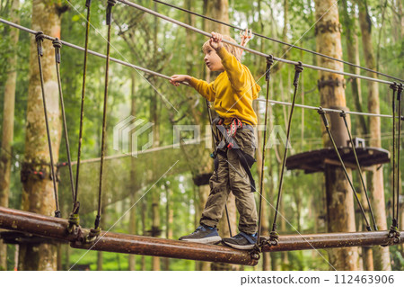 Little boy in a rope park. Active physical recreation of the child in the fresh air in the park. Training for children Little boy in a rope park. Active physical recreation of the child in the fresh air in the park. Training for children 112463906