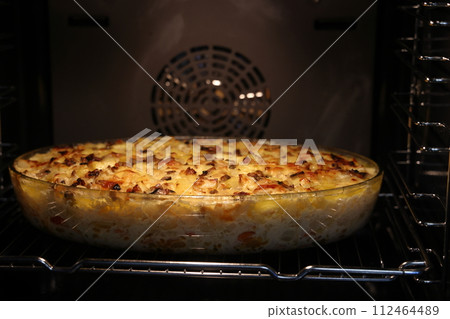 A mixture of fried vegetables is baked in the oven in a transparent dish. 112464489
